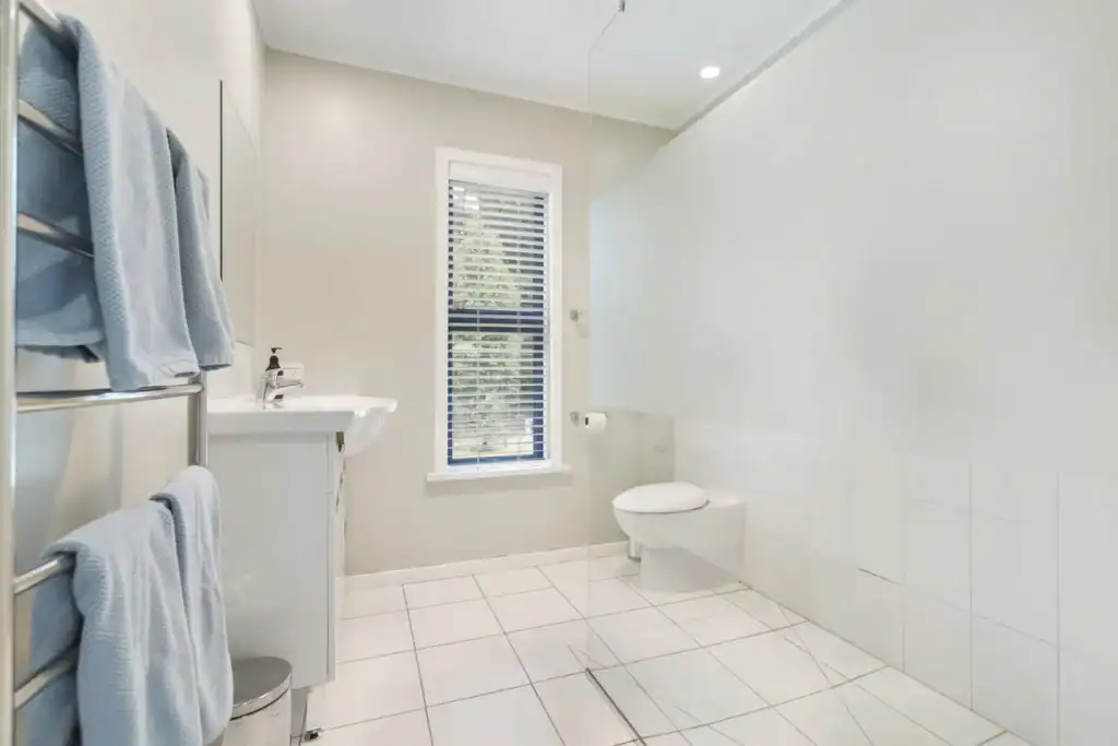 Bright modern bathroom interior at Judge & Jury Village, featuring a white toilet, sleek sink, and large window with blinds, perfect for comfortable stays.