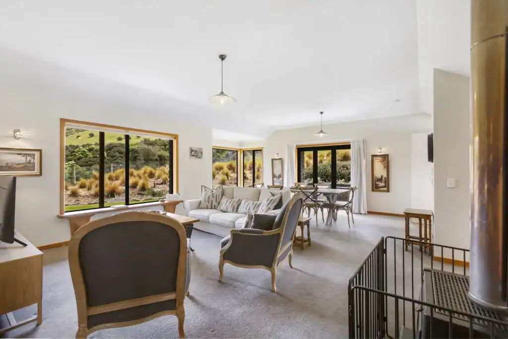 Cozy indoor living area at Judge & Jury Village, featuring large windows with scenic outdoor views, a comfortable sofa, and a dining table, perfect for relaxing and socializing.