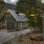 Charming modern barn-style accommodation at Judge & Jury Village with stone accents, outdoor seating, and ambient lighting surrounded by lush greenery and mountain scenery.