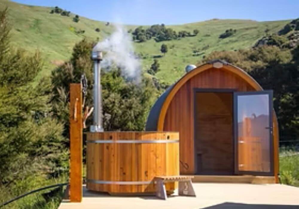 Rustic log cabin with outdoor deck, dining area, and BBQ grill at Judge & Jury Village, a unique retreat destination. Perfect for outdoor gatherings and scenic views in a natural setting.