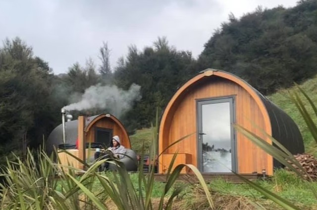 Judge & Jury Village mountain cabin in alpine scenery, surrounded by tall pine trees and a flowing creek, representing a rustic, natural setting for outdoor adventure and wilderness experiences.